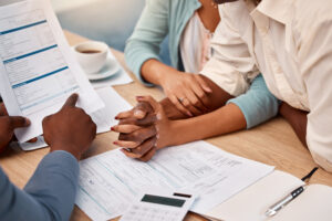Couple discussing insurance contract with advisor, paperwork and calculator on table, reflecting custom home financing consultation.